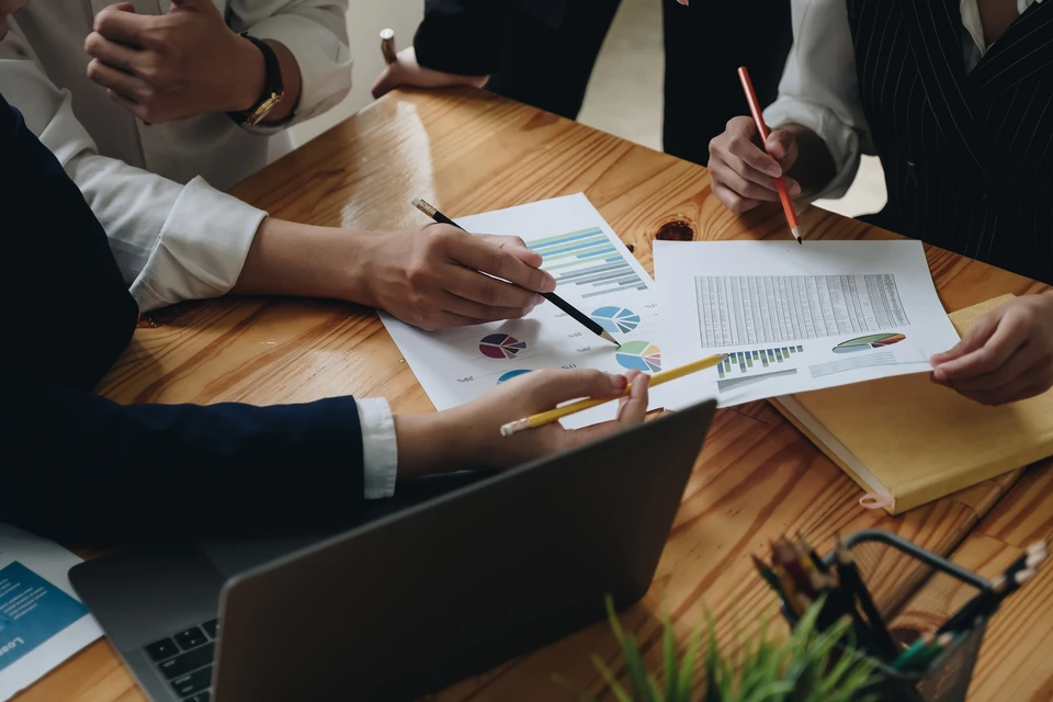 Réunion d'affaires dans un bureau avec trois professionnels analysant des documents financiers sur une table en bois